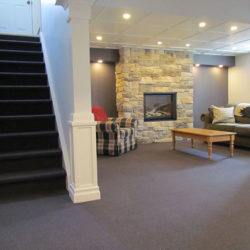 downstairs living room with large stone fireplace, stairwell adjacent